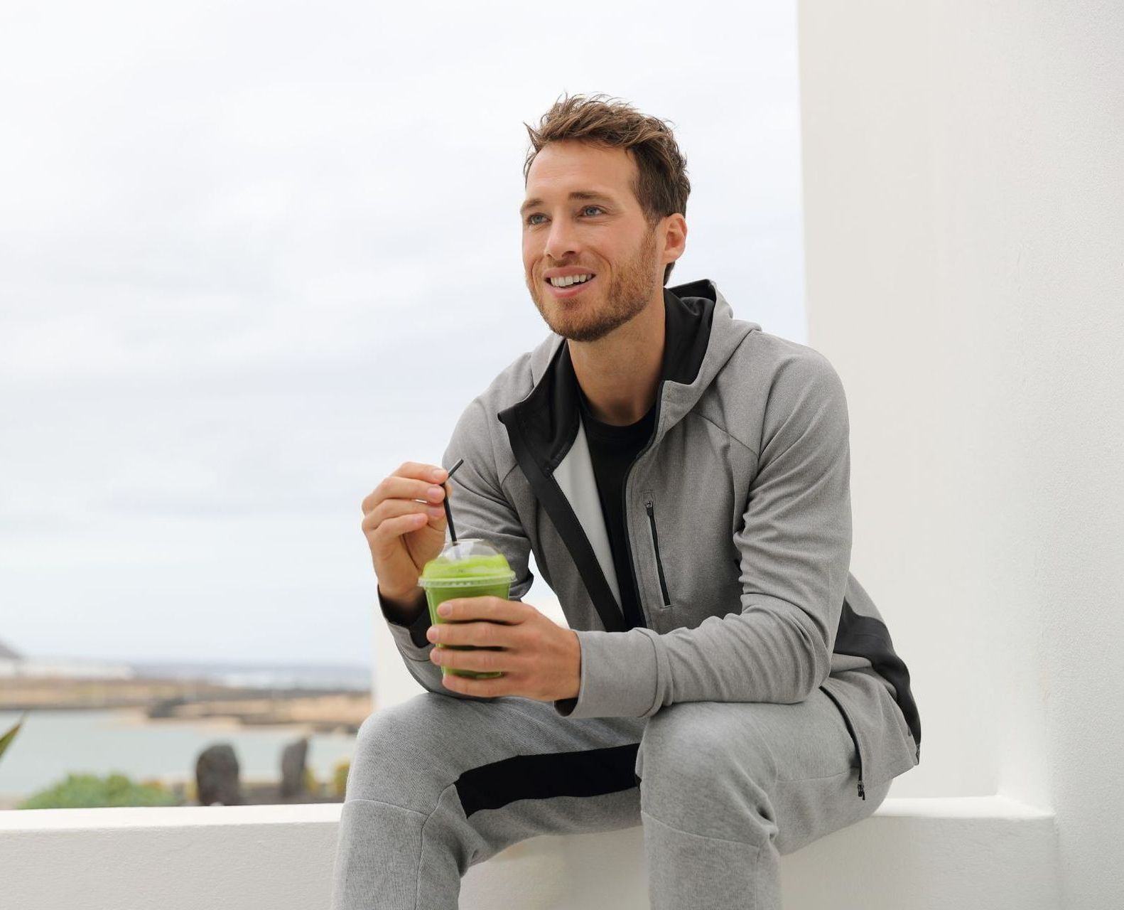 young man in athletic clothes sitting drinking green smoothie