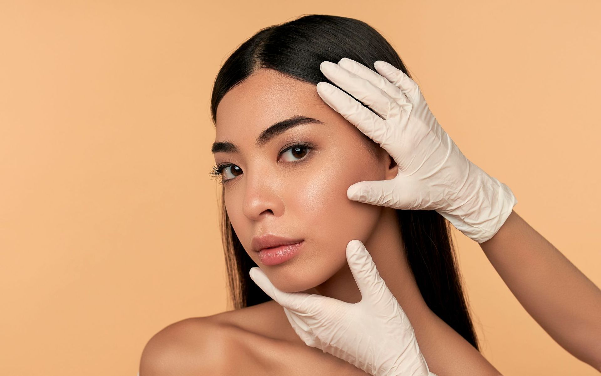 beautiful young woman with doctor's gloved hands on face prepping for aesthetic treatment