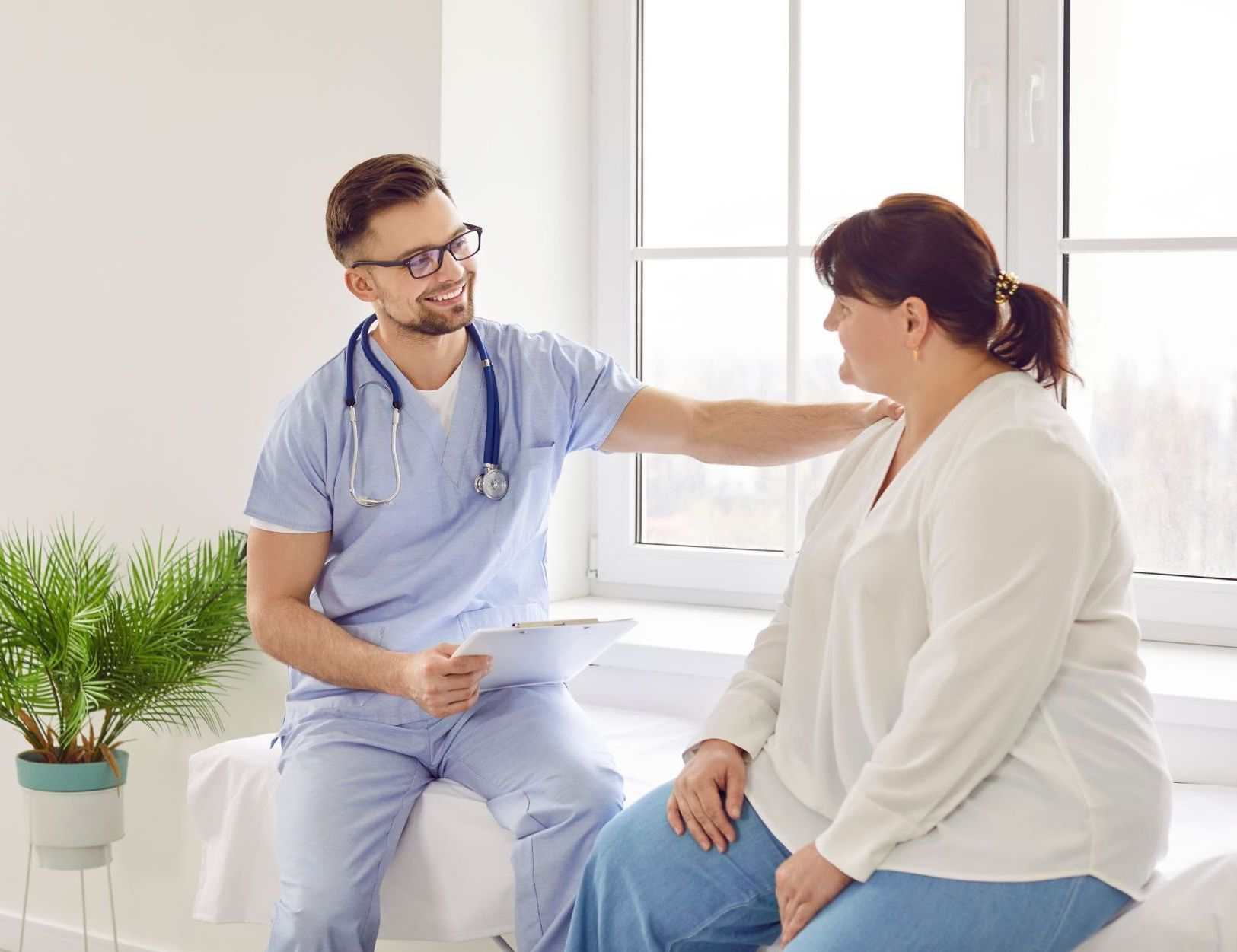 young male doctor in blue scrubs discussing care with overweight female patient