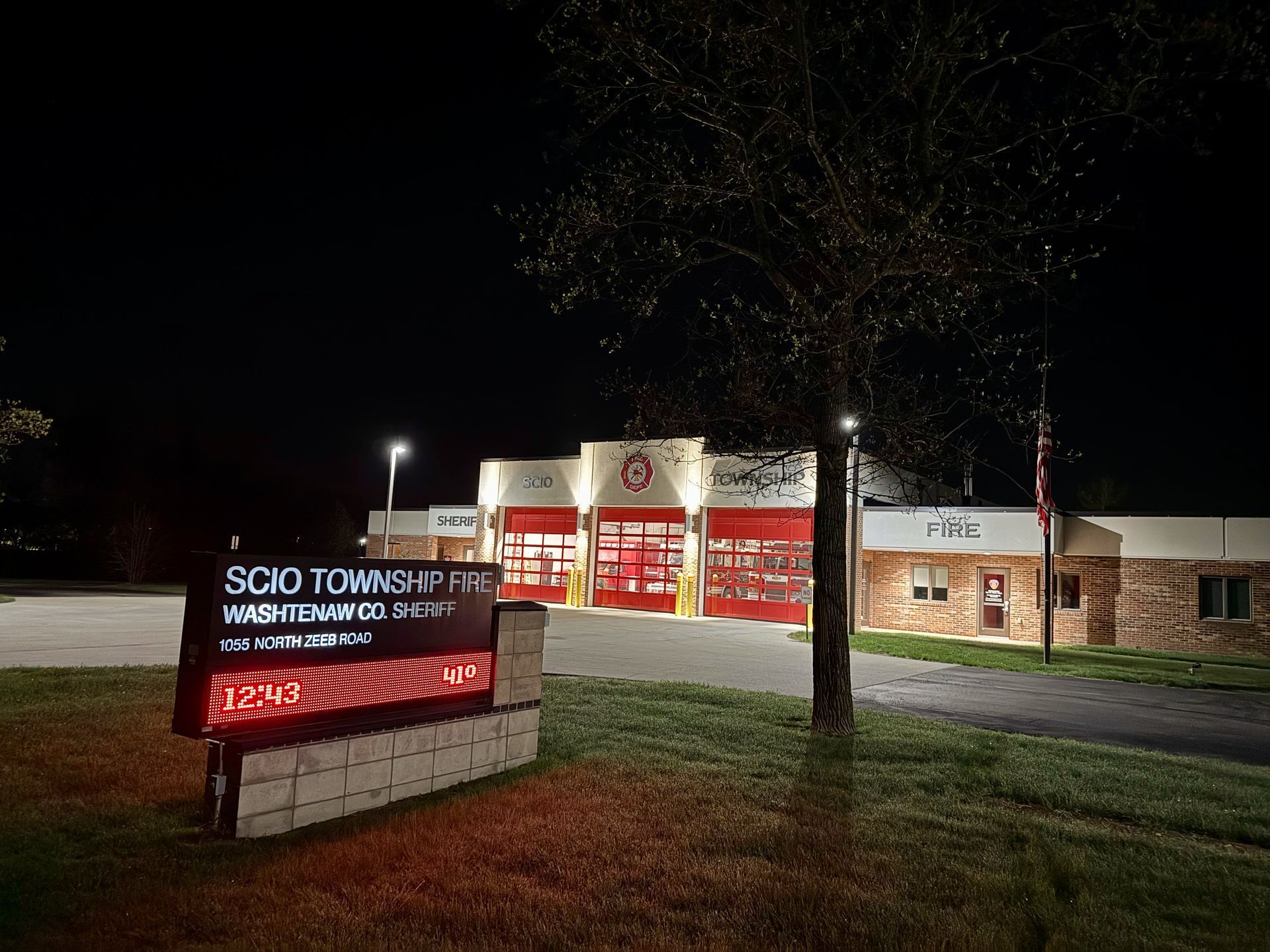 A fire station is lit up at night with a sign in front of it.