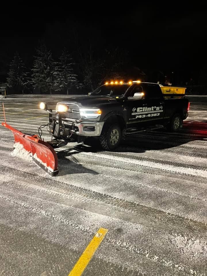A truck is plowing snow in a parking lot at night.