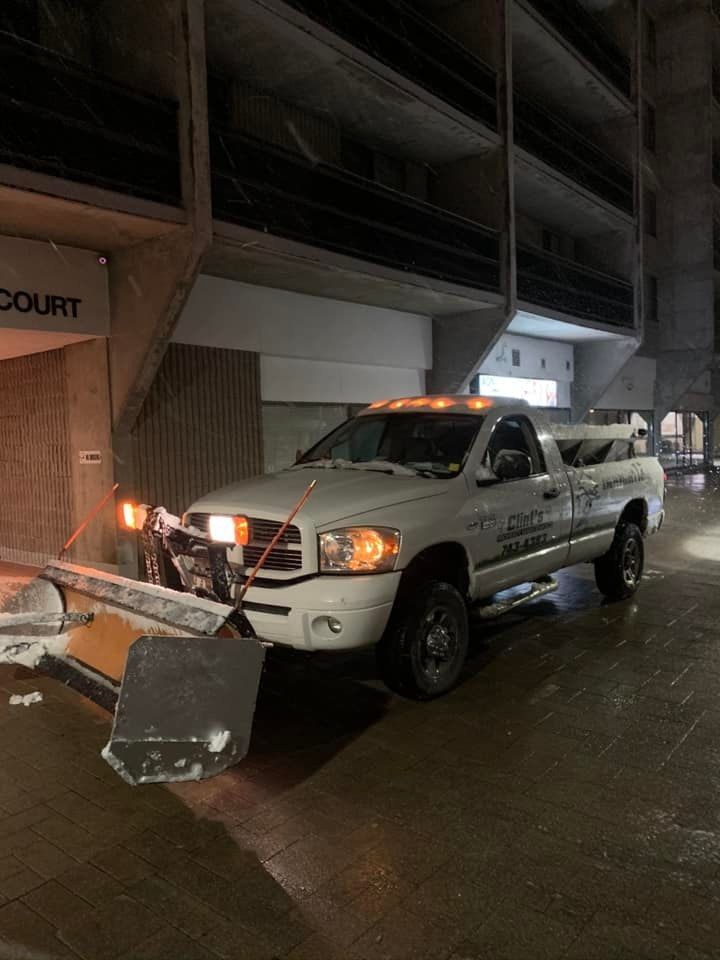 A white truck with a snow plow attached to the front is parked in front of a building.