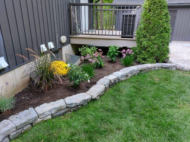A lush green lawn with a stone border and flowers in front of a house.