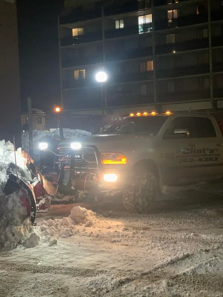 A snow plow is clearing snow from a parking lot at night.