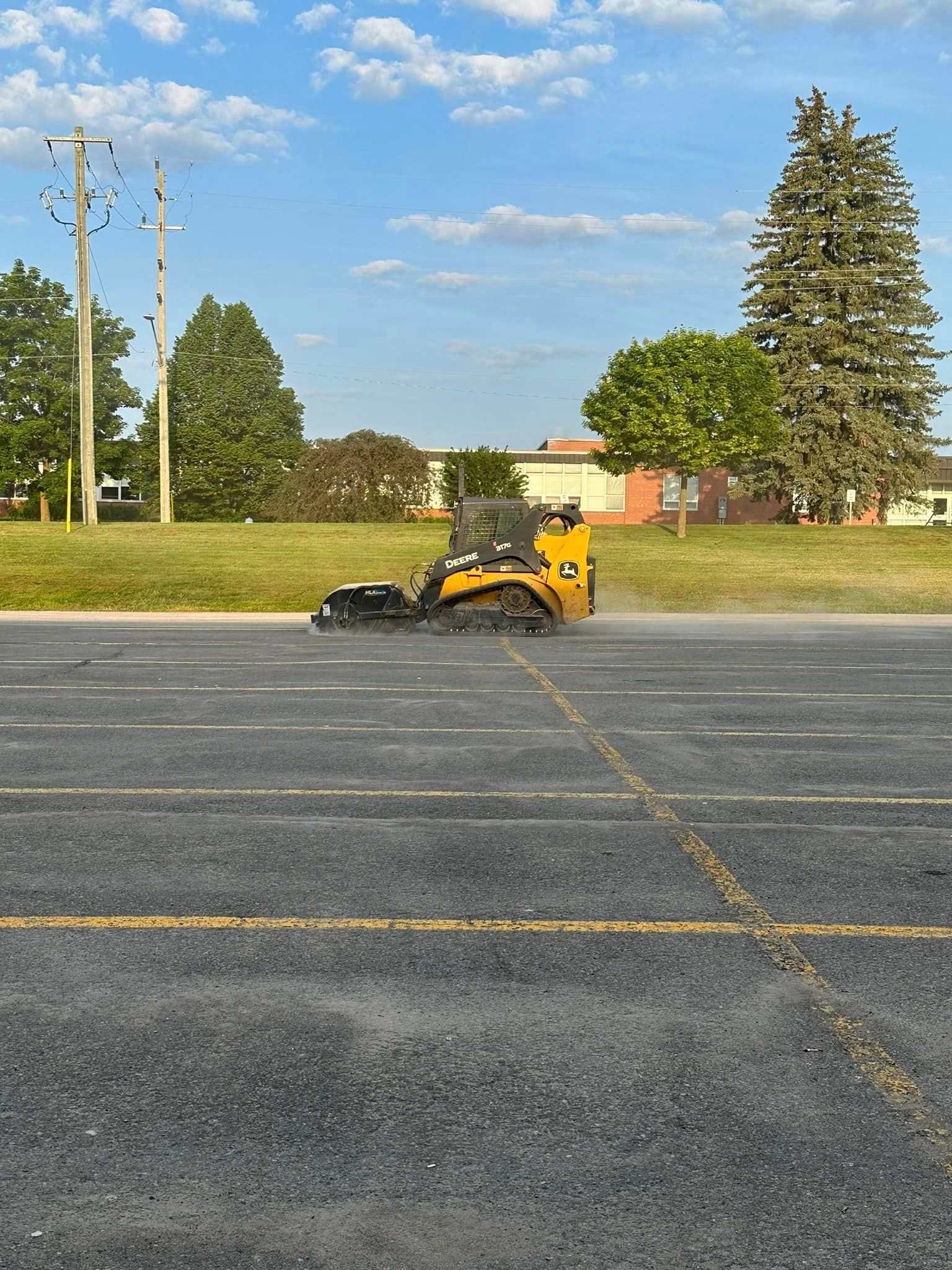 A yellow tractor is cutting grass in a parking lot.