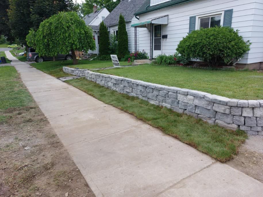 A sidewalk leading to a house with a stone wall in front of it.