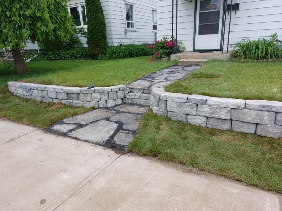 A stone walkway leading to a house with a stone wall.