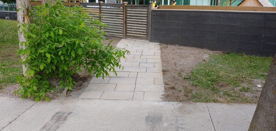 A brick walkway leading to a black fence and a house.