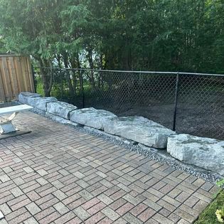 A brick patio with a chain link fence and rocks.