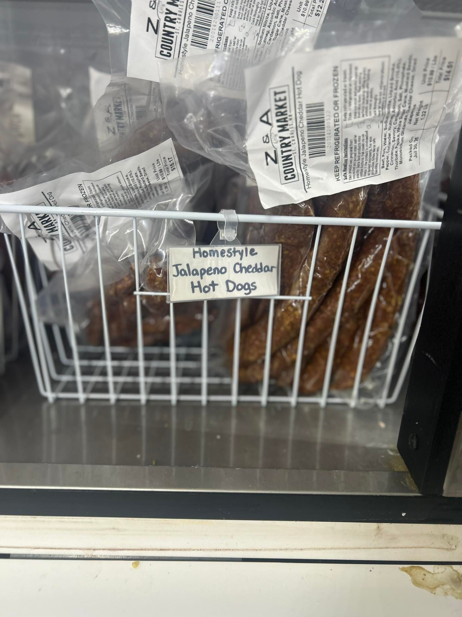 Jalapeño cheddar hot dogs in a wire basket at a market, in a refrigerated display case.