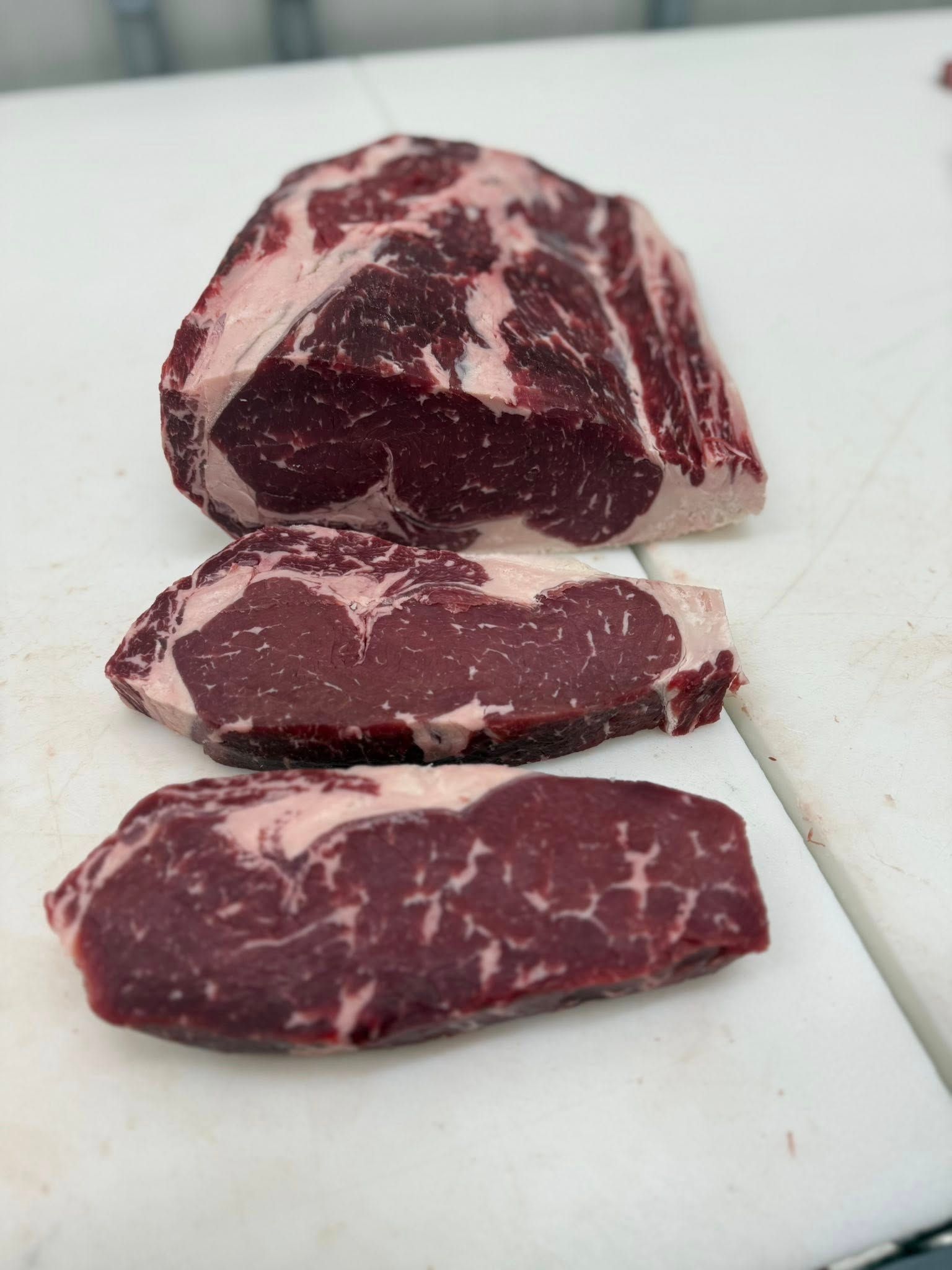 Three cuts of raw steak, varying in size, on a white cutting board.
