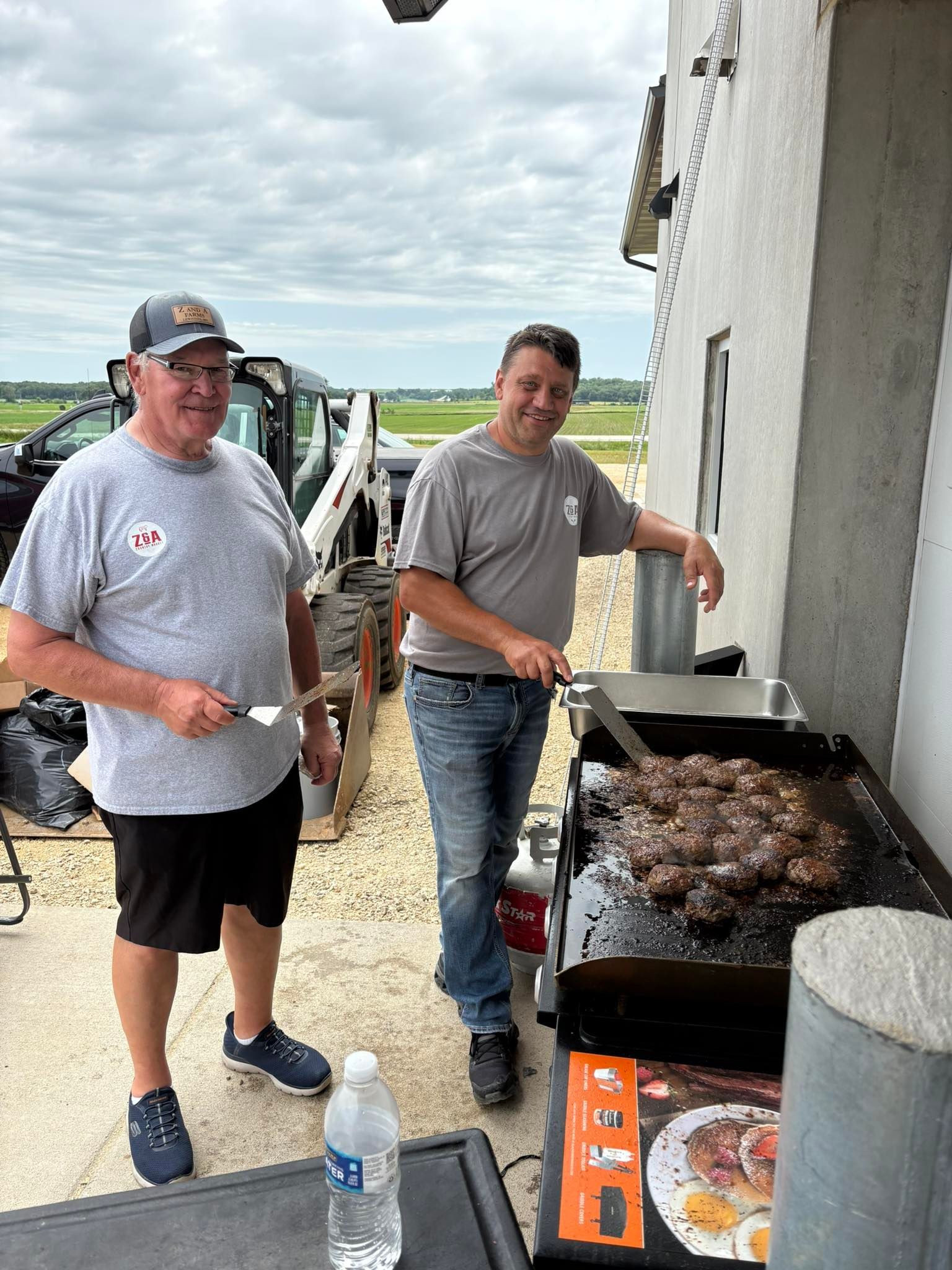 Two men grilling burgers outdoors on a cloudy day.
