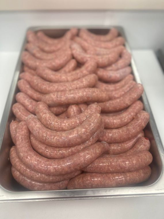 Tray filled with rows of uncooked sausages, light pink in color, on a metal tray.