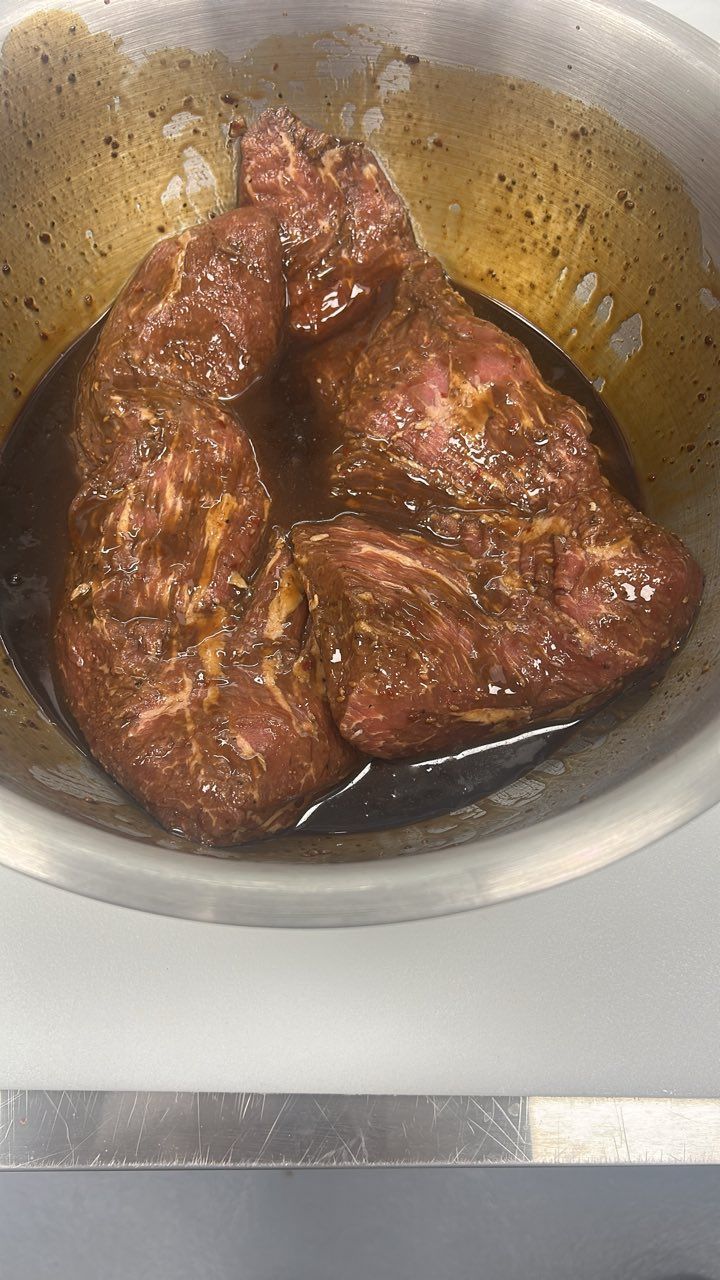 Marinated steak pieces in a metal bowl; dark brown marinade coats the red meat.