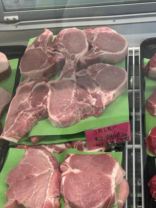 Raw pork chops displayed in a butcher shop's refrigerated case, on green paper.