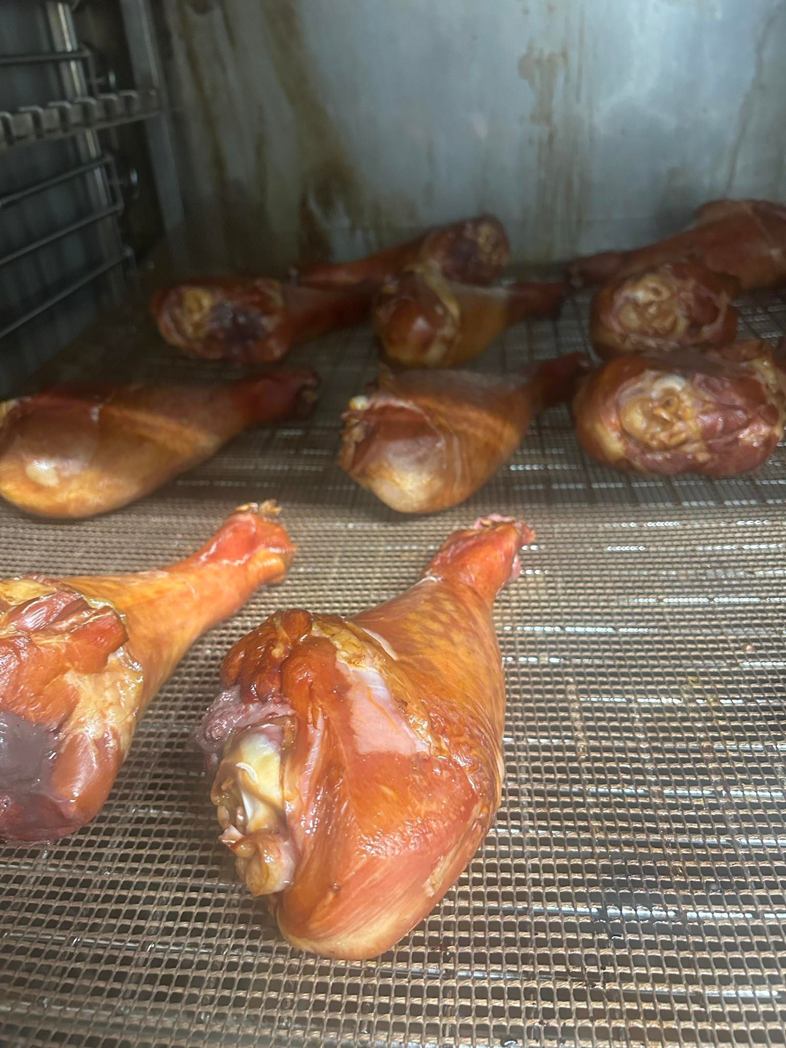 Smoked turkey legs in a smoker, golden brown with glistening skin, on metal racks.