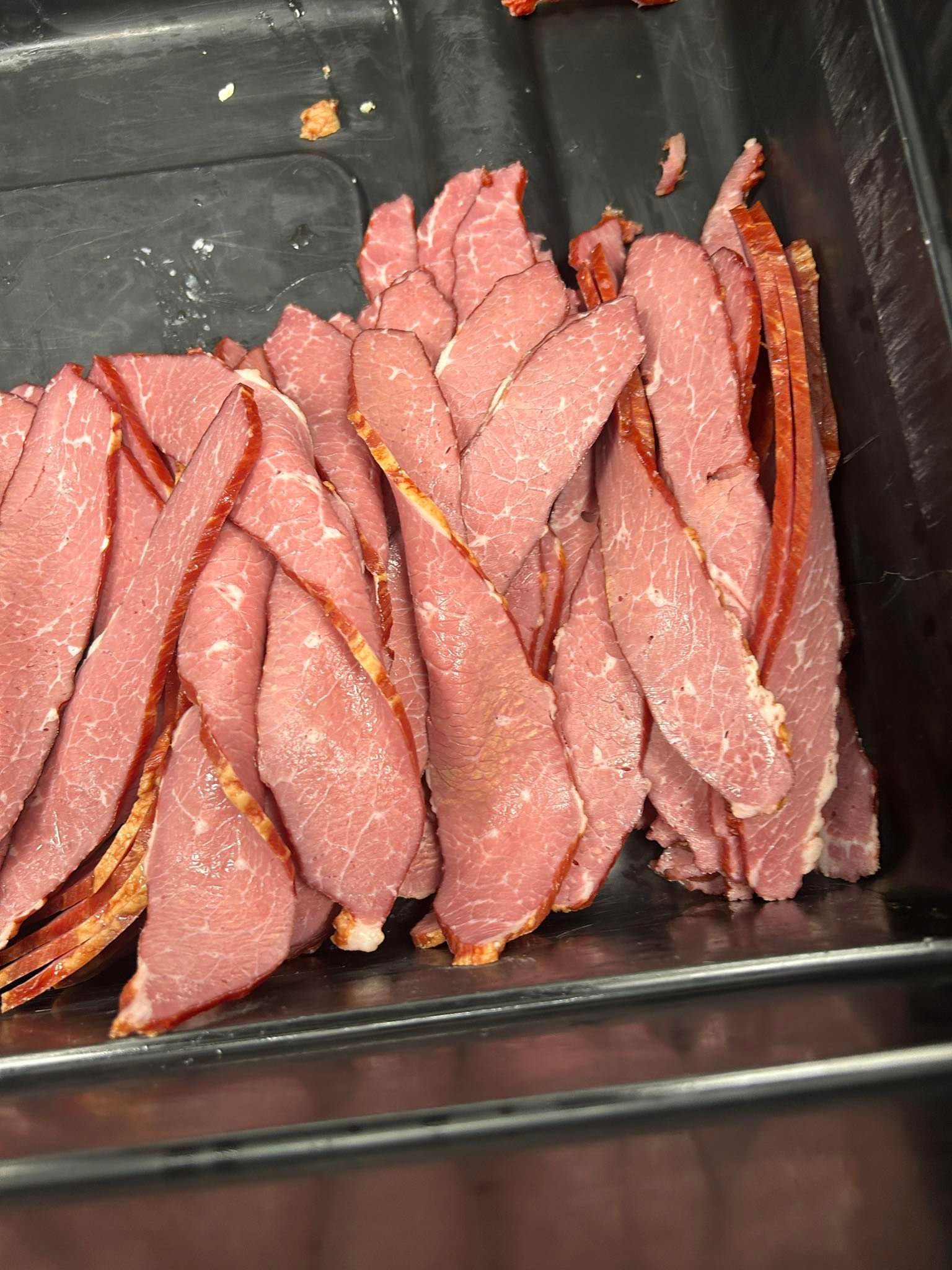 Thinly sliced corned beef arranged in a tray, with red-brown coloring and visible fat.