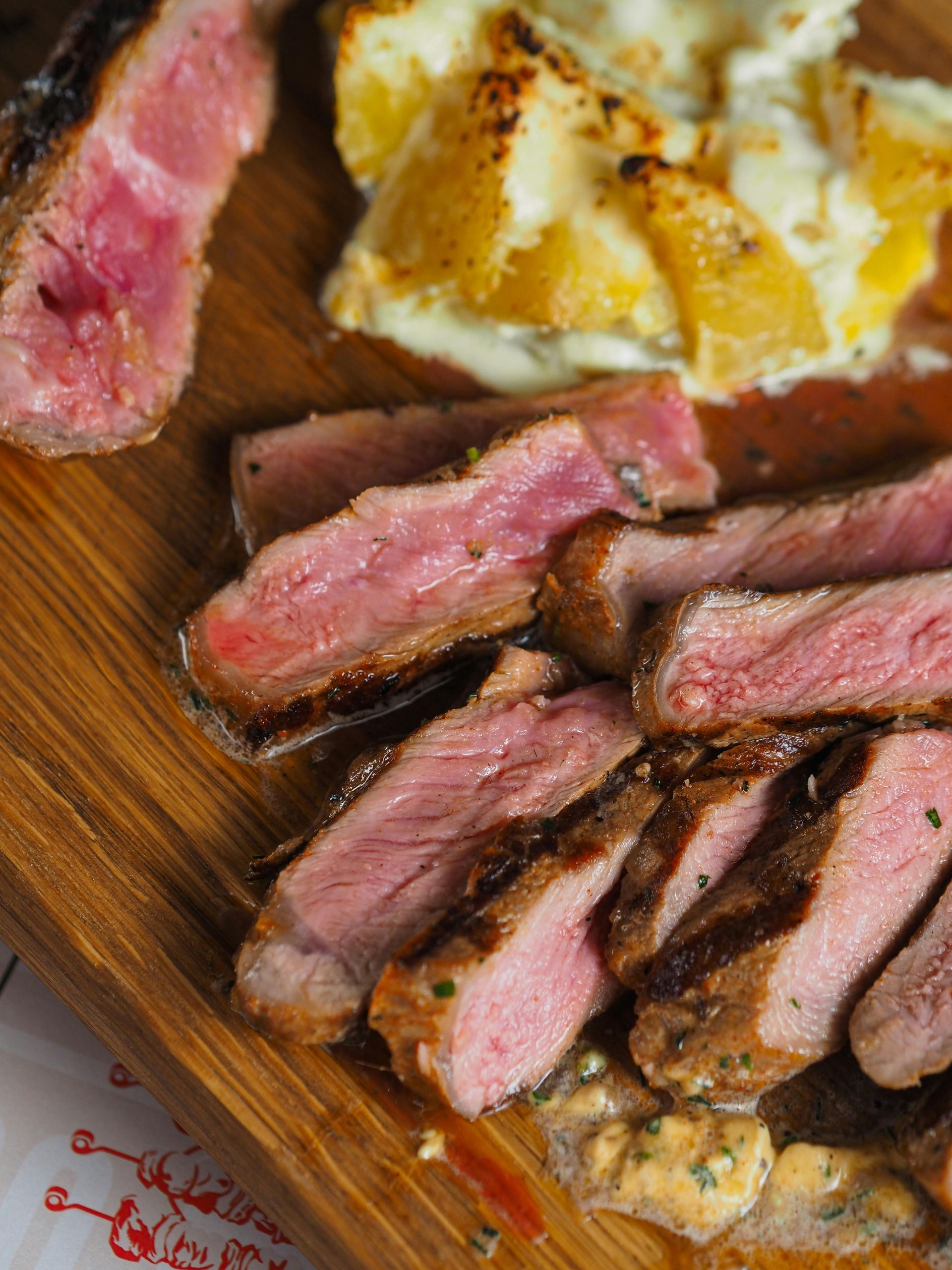 Sliced medium-rare steak on a wooden board with roasted potatoes and sauce.