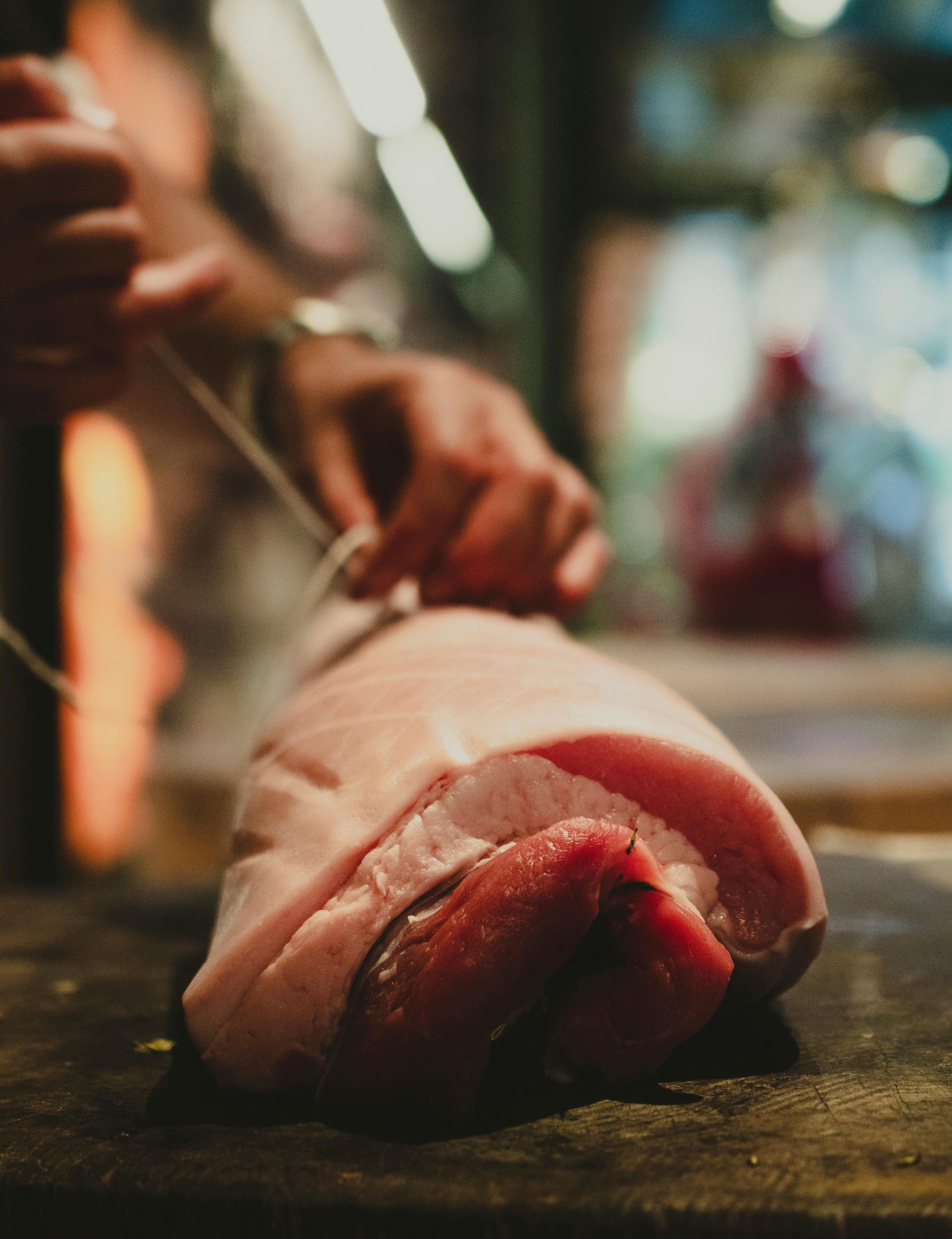 A chef ties twine around a raw pork roast on a dark wooden surface, with blurred background.