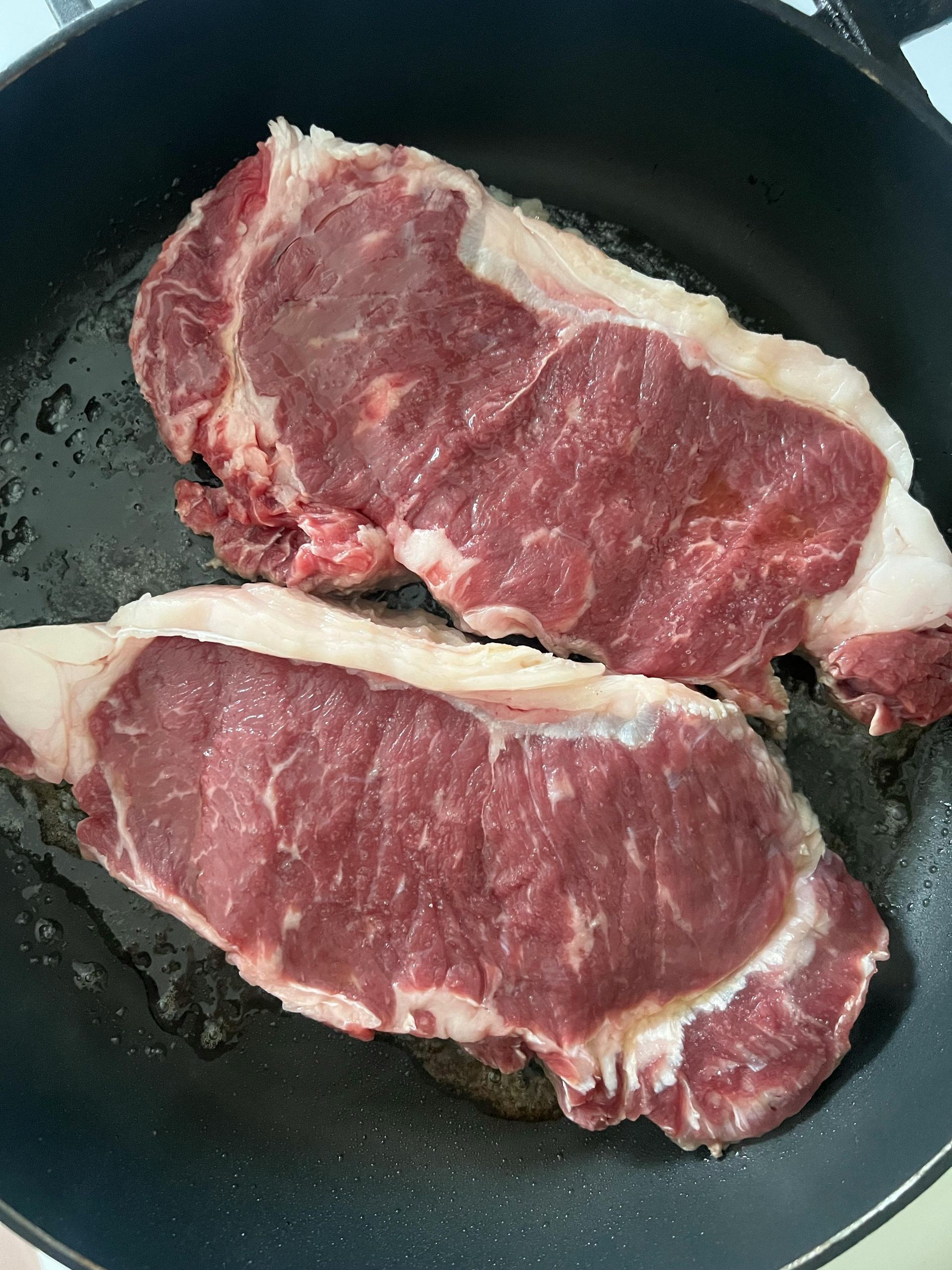 Two raw steaks searing in a black frying pan.