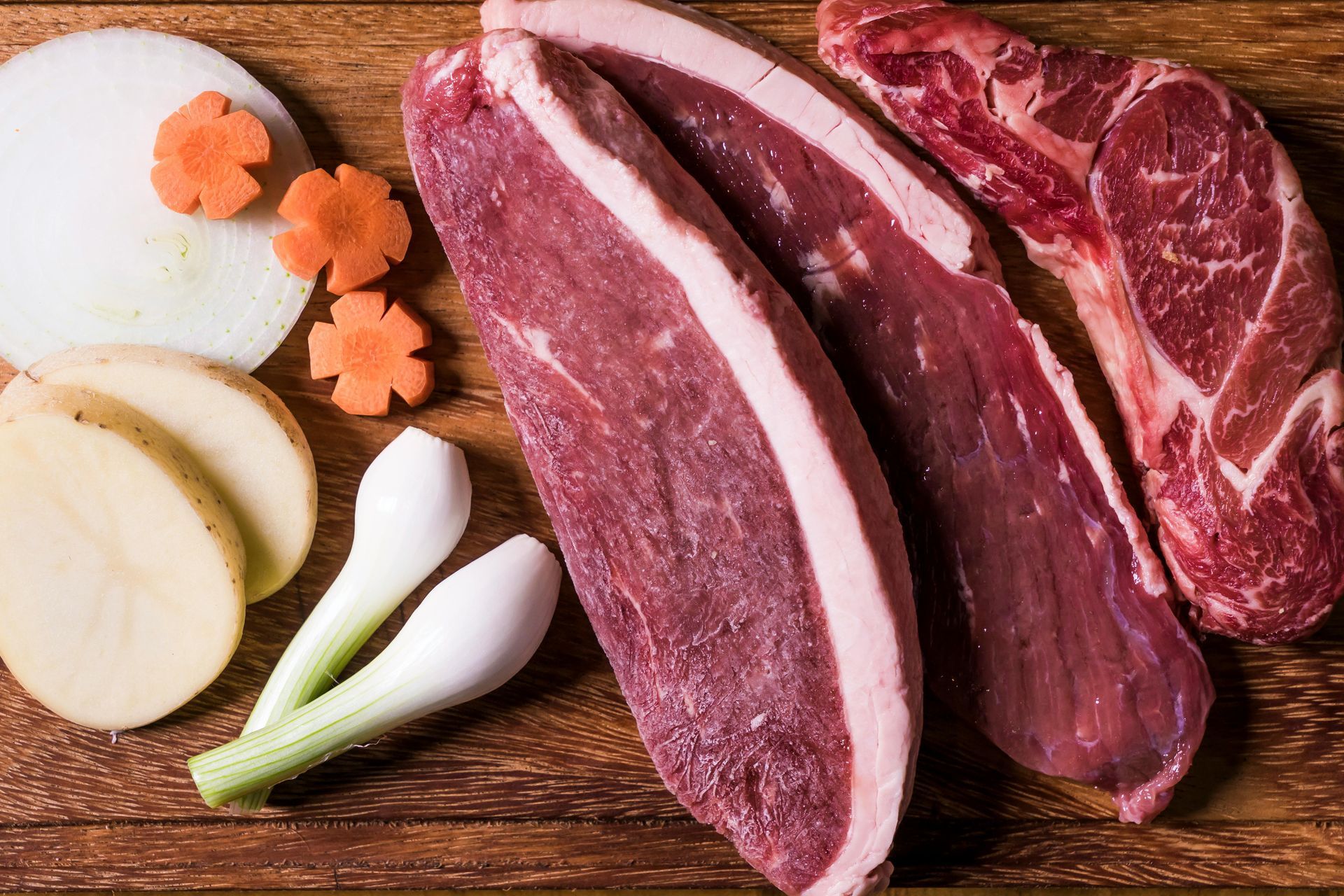 Raw meat and sliced vegetables on a wooden cutting board; ingredients for cooking.