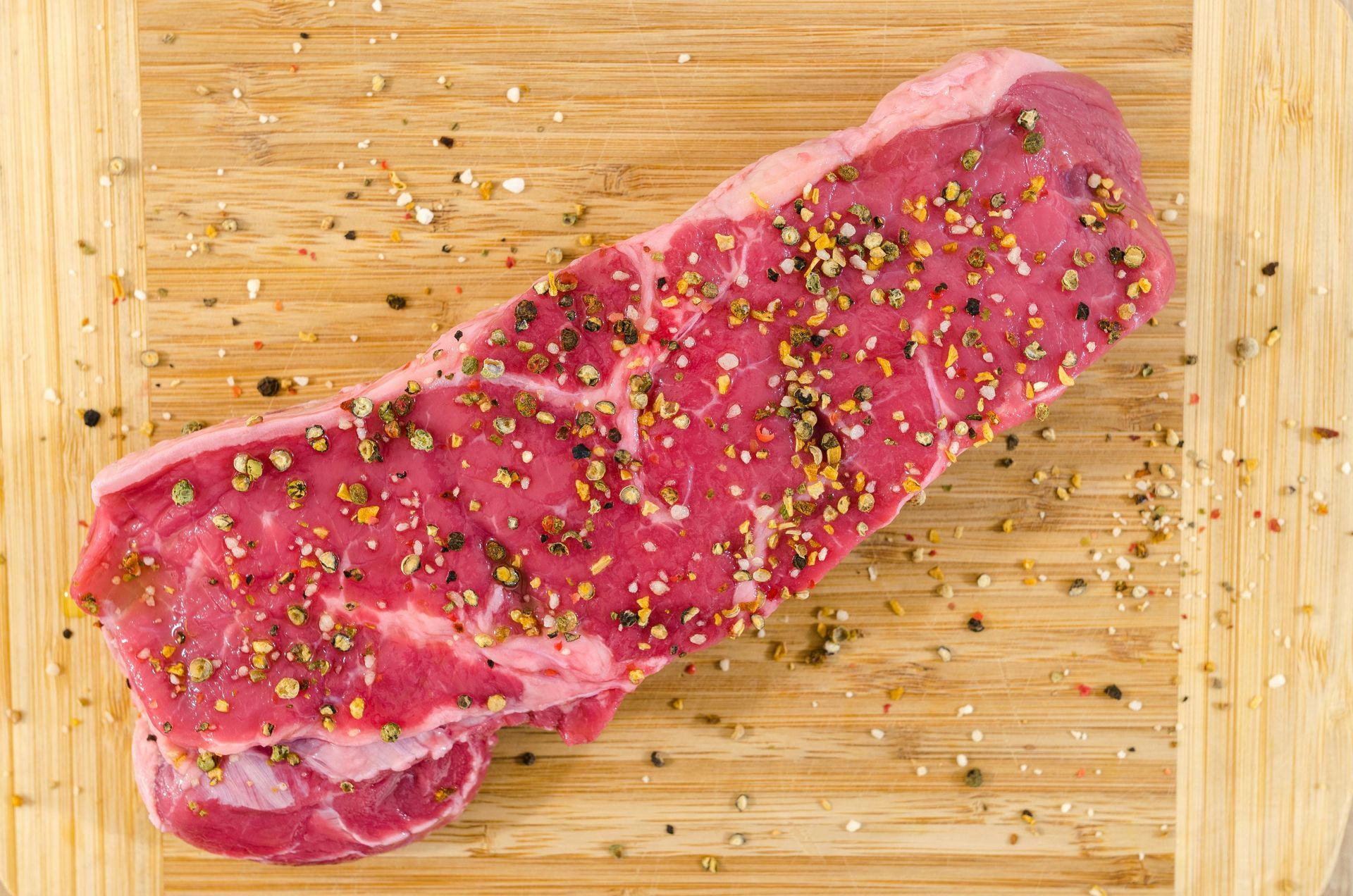 Raw seasoned steak on a wooden cutting board.