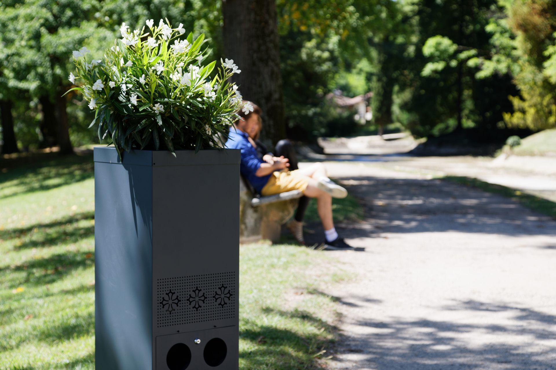 Un homme est assis sur un banc dans un parc à côté d'une poubelle.