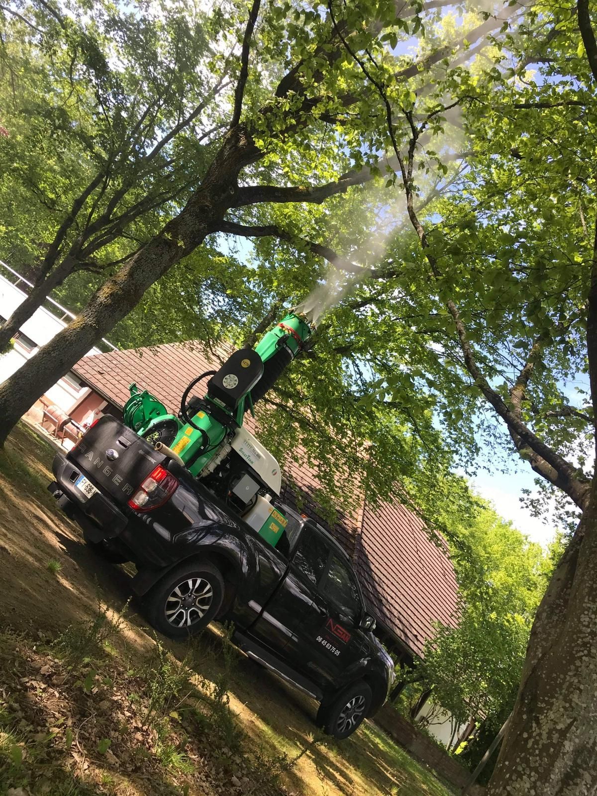 Un camion pulvérise des arbres avec une machine à l'arrière.