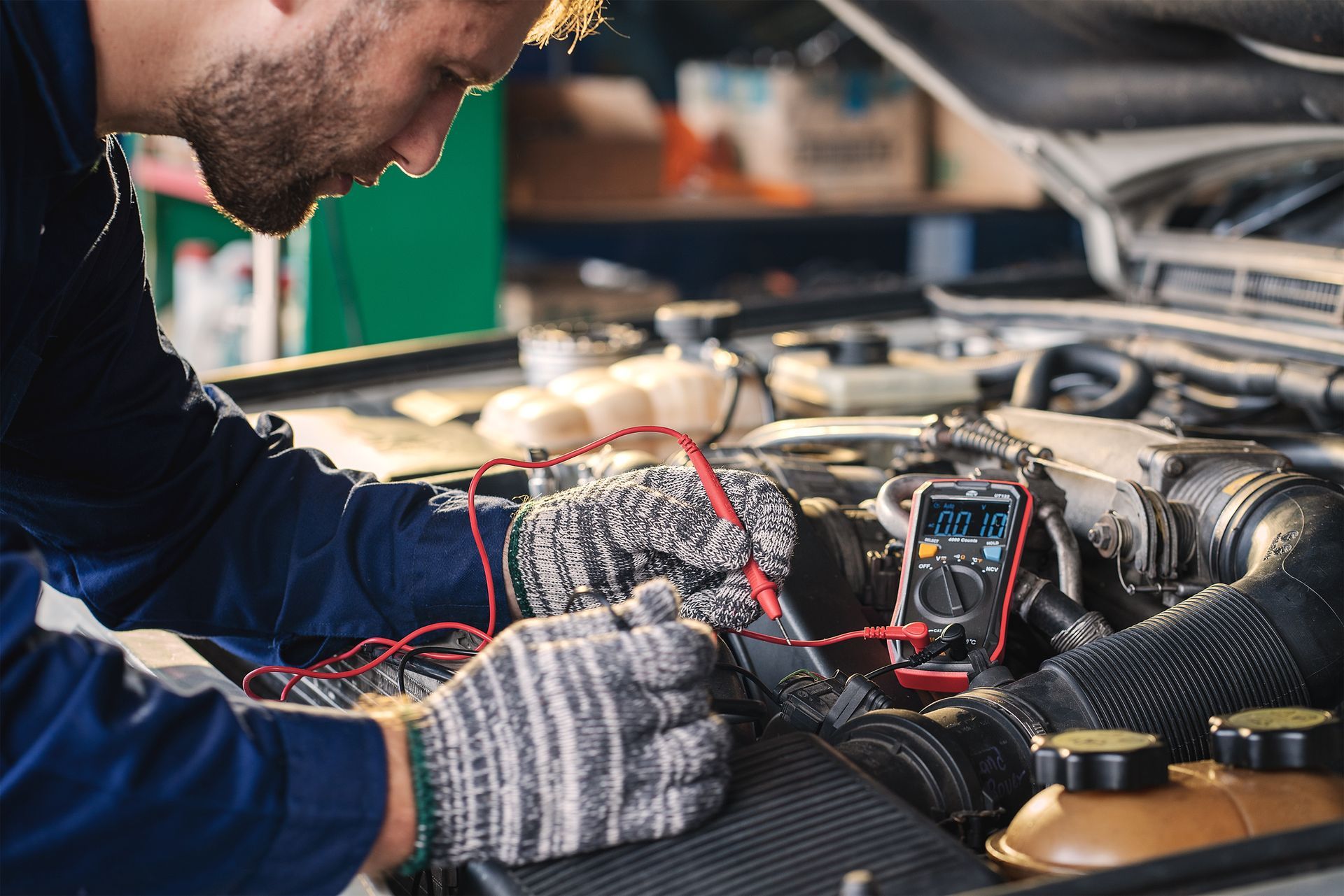 A man is working on a car engine with a multimeter.
