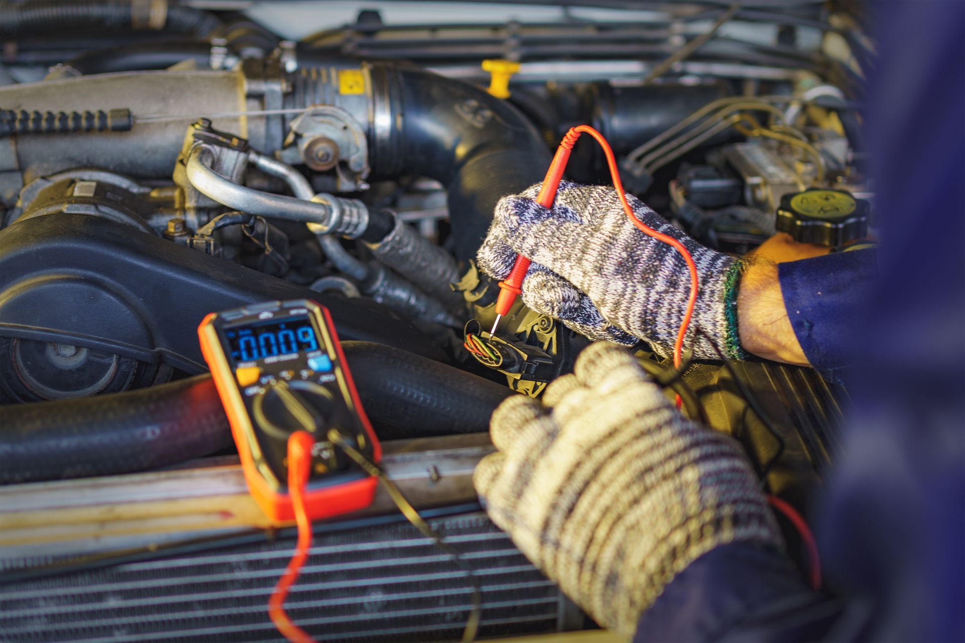 A mechanic is working on a car engine with a multimeter.