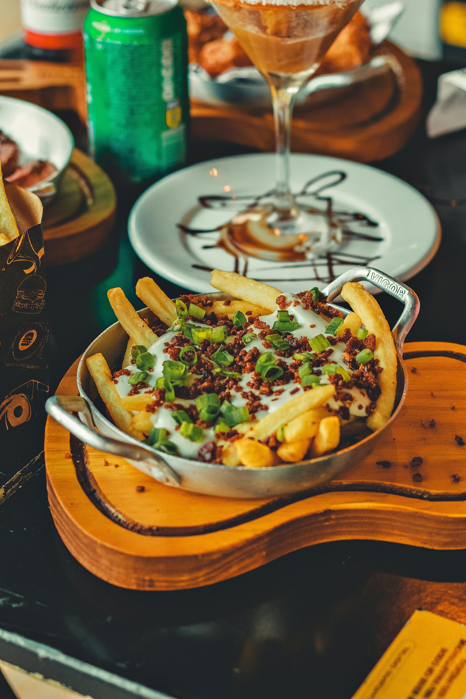 Frietjes met kaas, spek en lente-uitjes, geserveerd op een houten plank in een restaurant.
