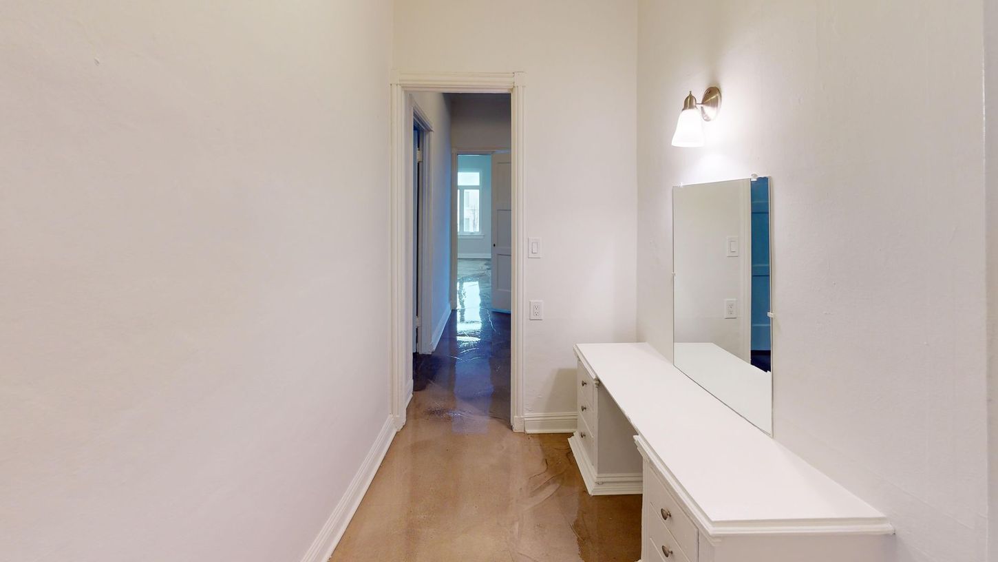 Hallway with a white vanity and mirror, wooden floor. Doorway at end.