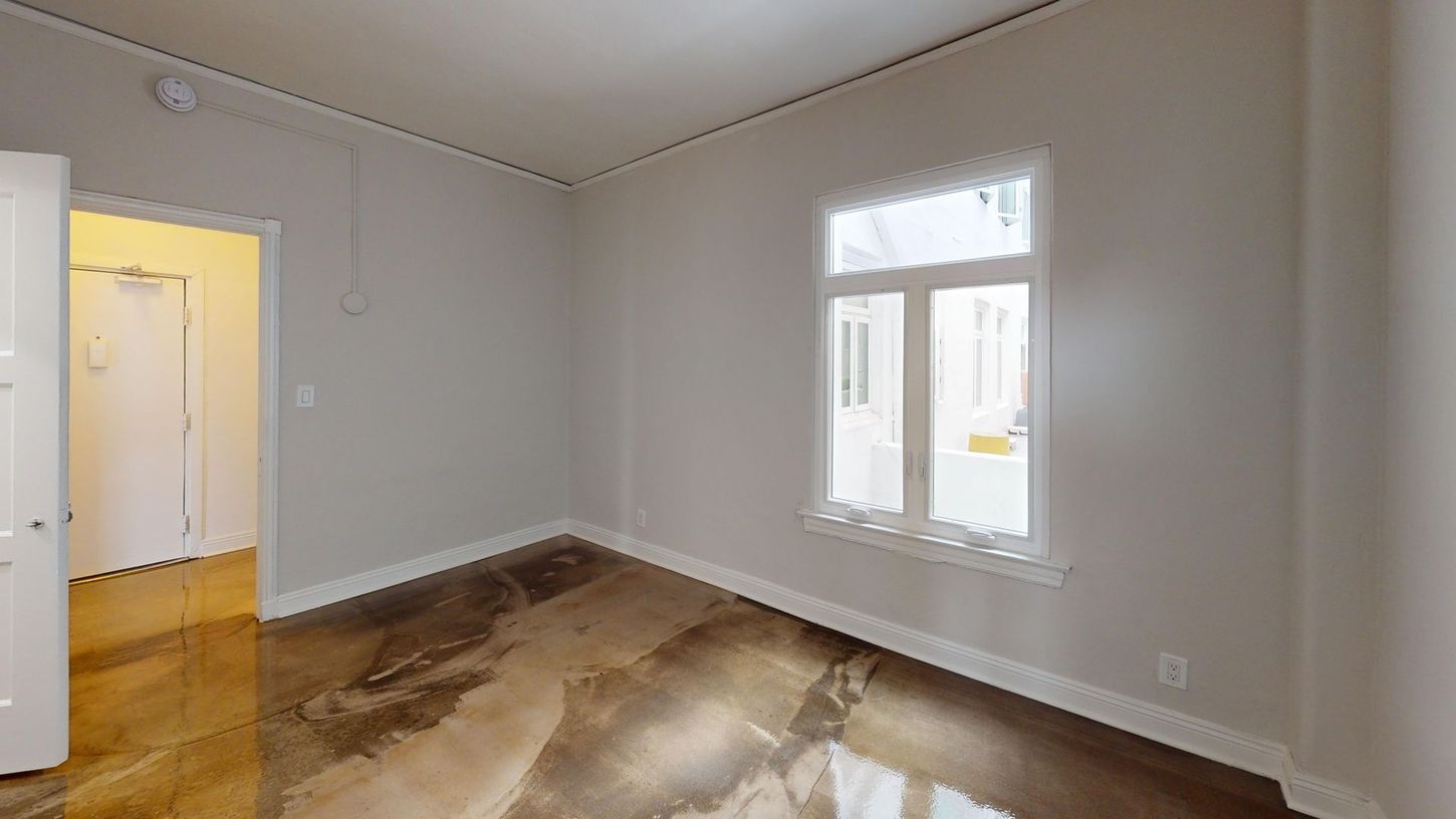 Empty room with window and doorway; concrete floor, light gray walls.