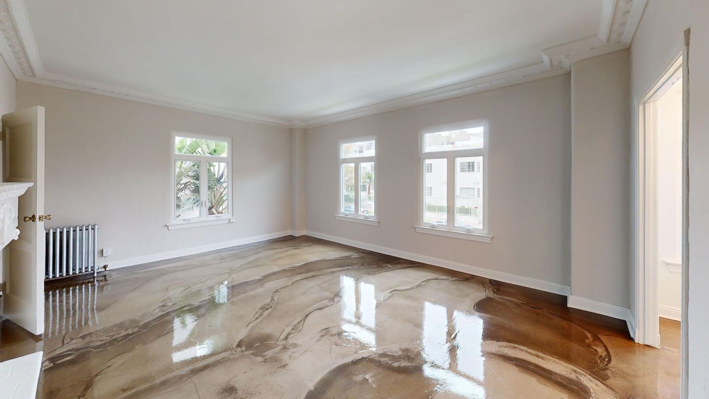 Empty room with glossy, marbled-looking floor and windows. White walls, trim, and a radiator. Open doorway.