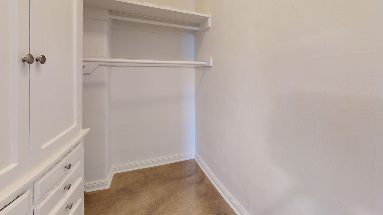 Empty white closet with a rod and shelf, carpeted floor.