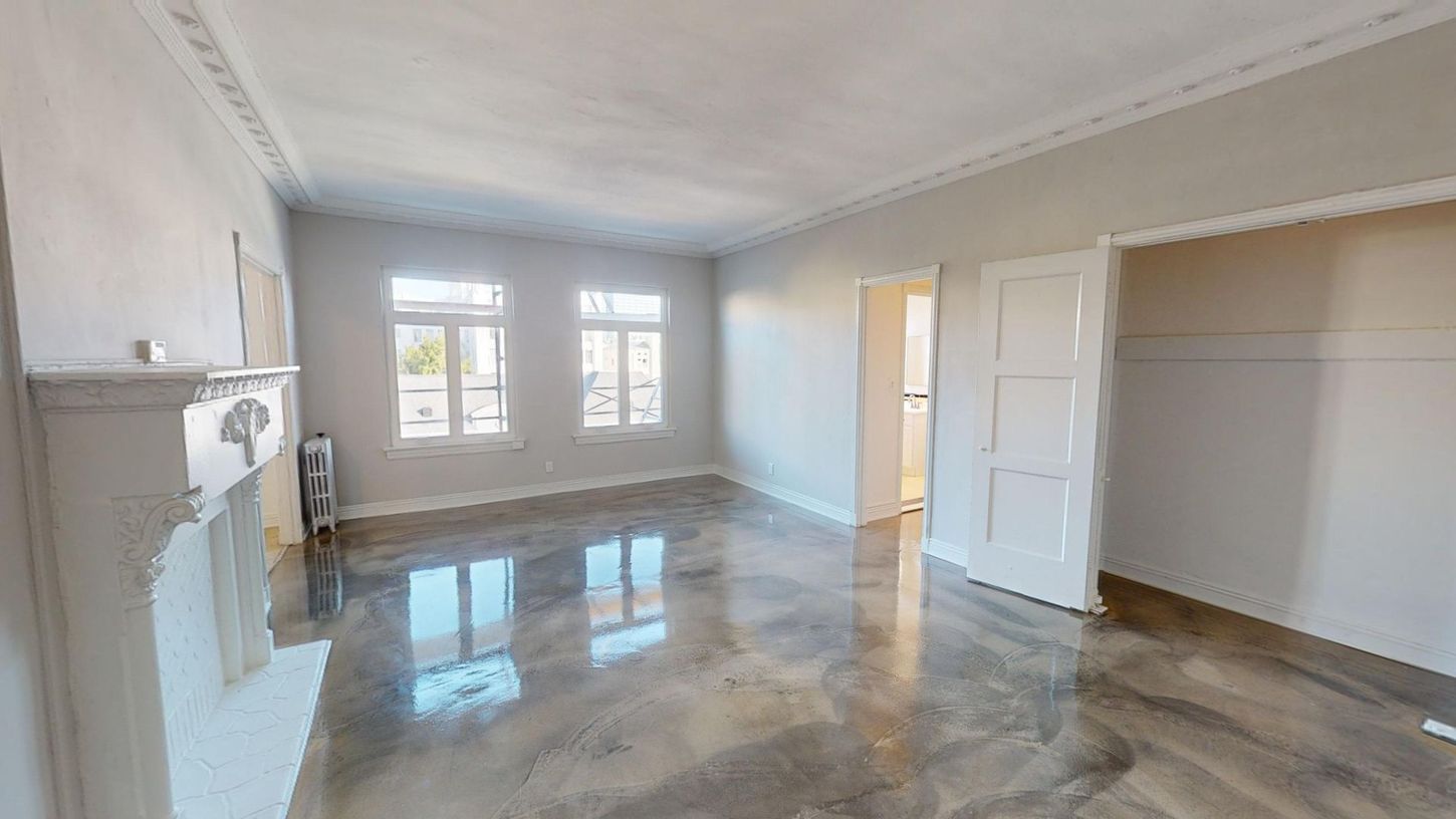 Empty room with shiny gray floor, white trim, fireplace, and windows.
