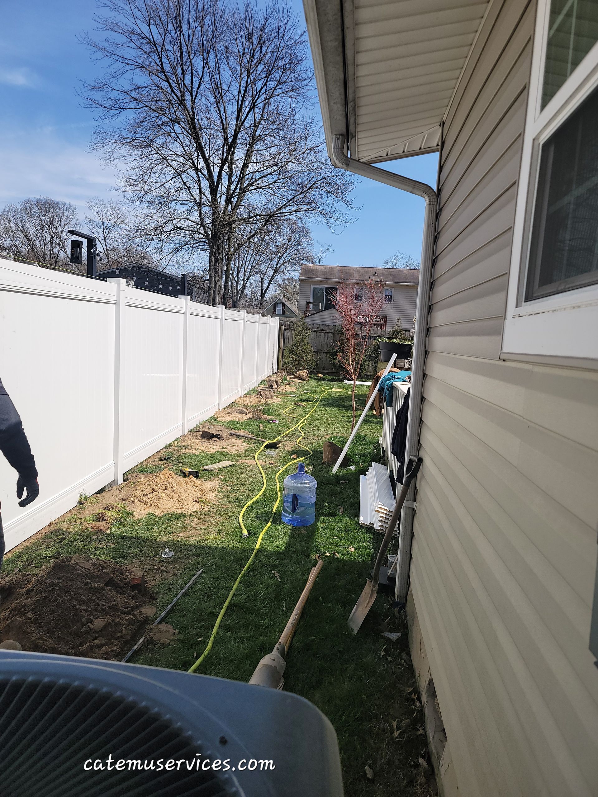 Backyard with a white fence, side of a house, and yard work in progress.