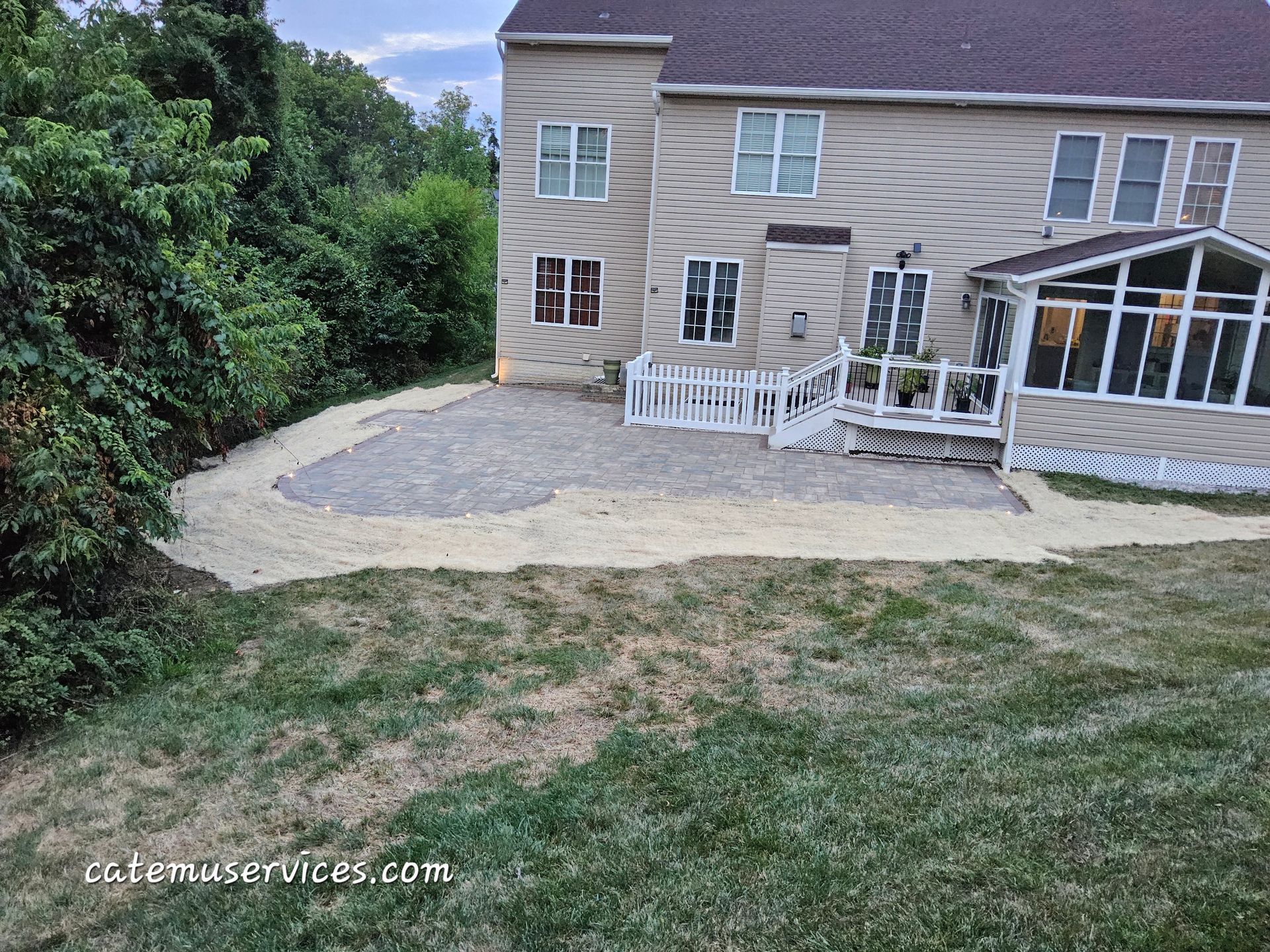 Backyard patio with gravel base, adjacent to house, white picket fence, and sunroom.