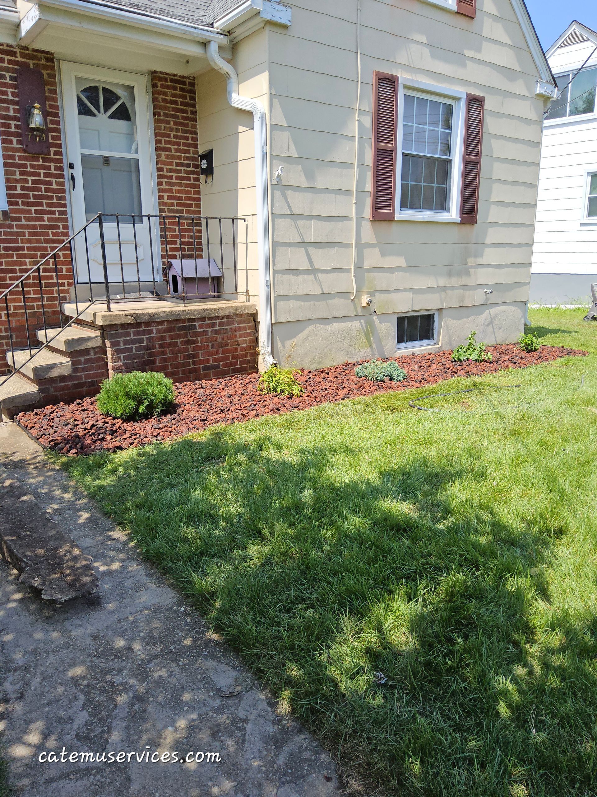 A house with red brick and tan siding, a red mulch flowerbed, and a patch of green grass.