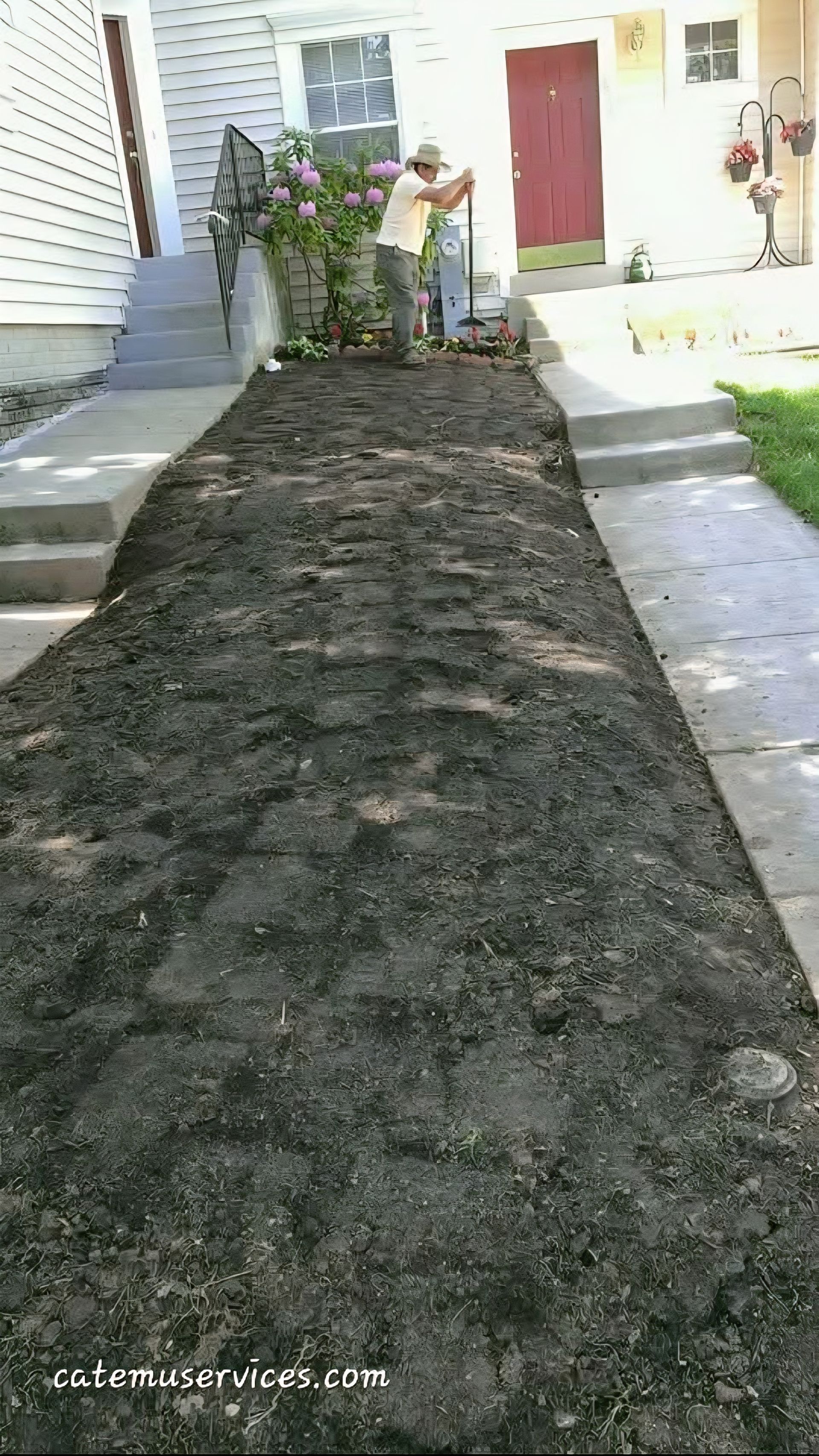 Person gardening a narrow strip of dark soil between concrete walkways, with buildings in the background.