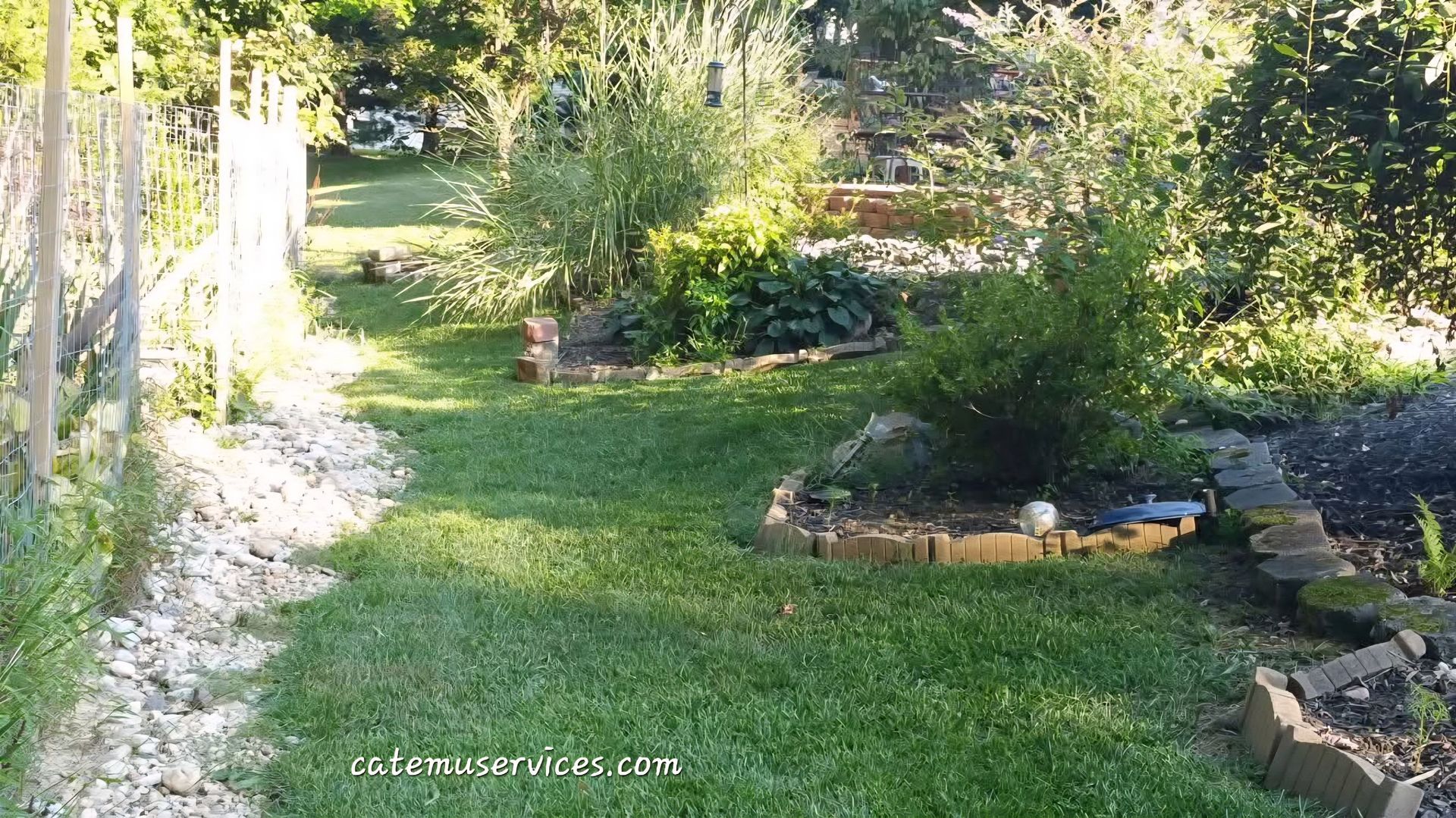 Lush garden with green grass, brick borders, various plants, and sunlight.