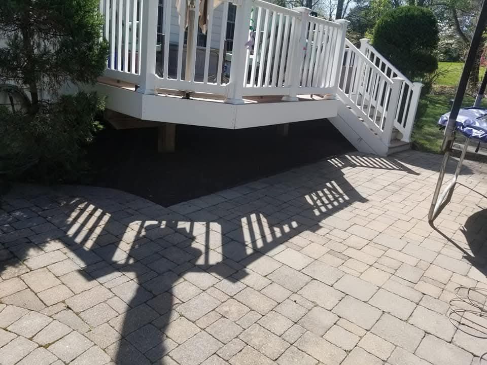 White deck with stairs casting a shadow on a brick patio. Dark mulch beneath deck.