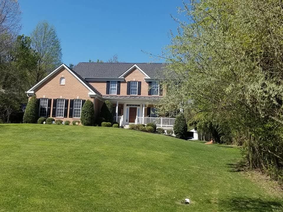 Two-story brick house with black shutters, white porch, and green lawn under a blue sky.