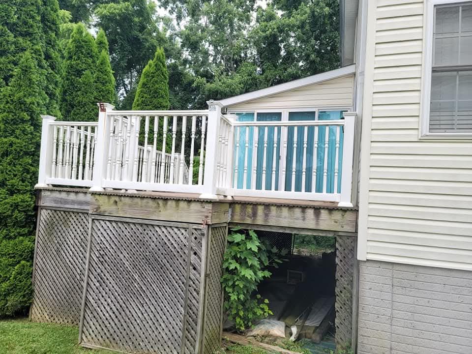 White deck with lattice underneath, attached to a light-colored house. Green trees and grass surround it.