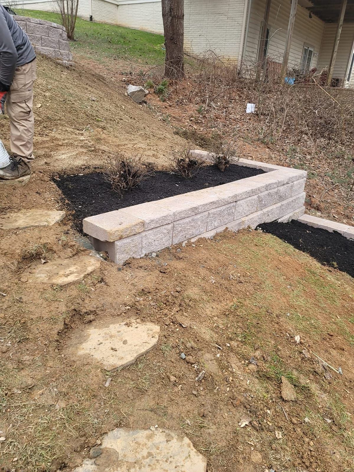 Stone retaining wall construction on a hillside. Stepping stones and mulch are present.