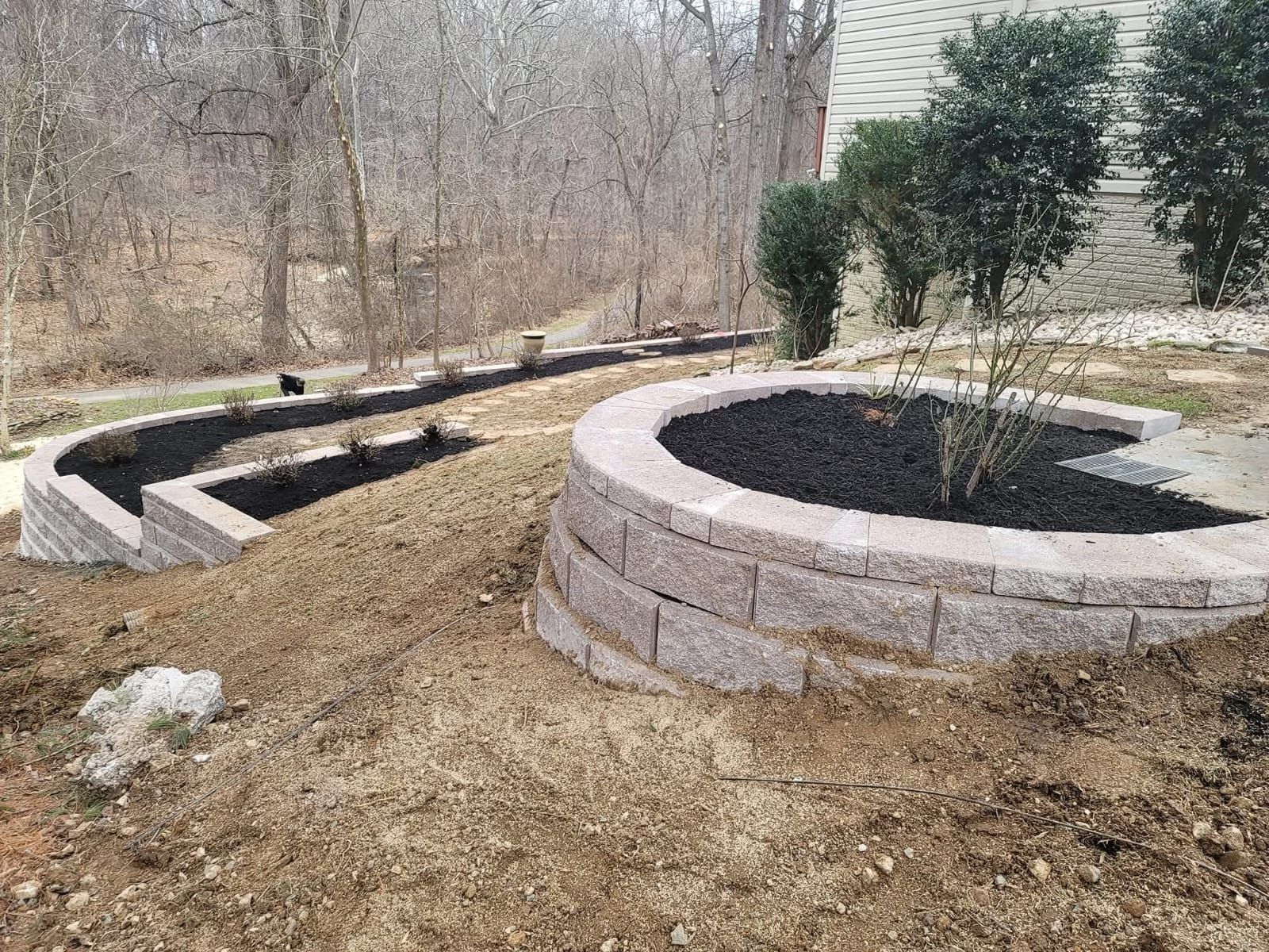 A multi-tiered landscape with brick retaining walls and circular flower beds filled with mulch and plants.
