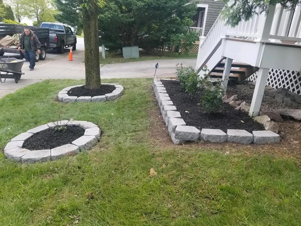 Landscaped yard with stone borders, mulched beds, and person walking.