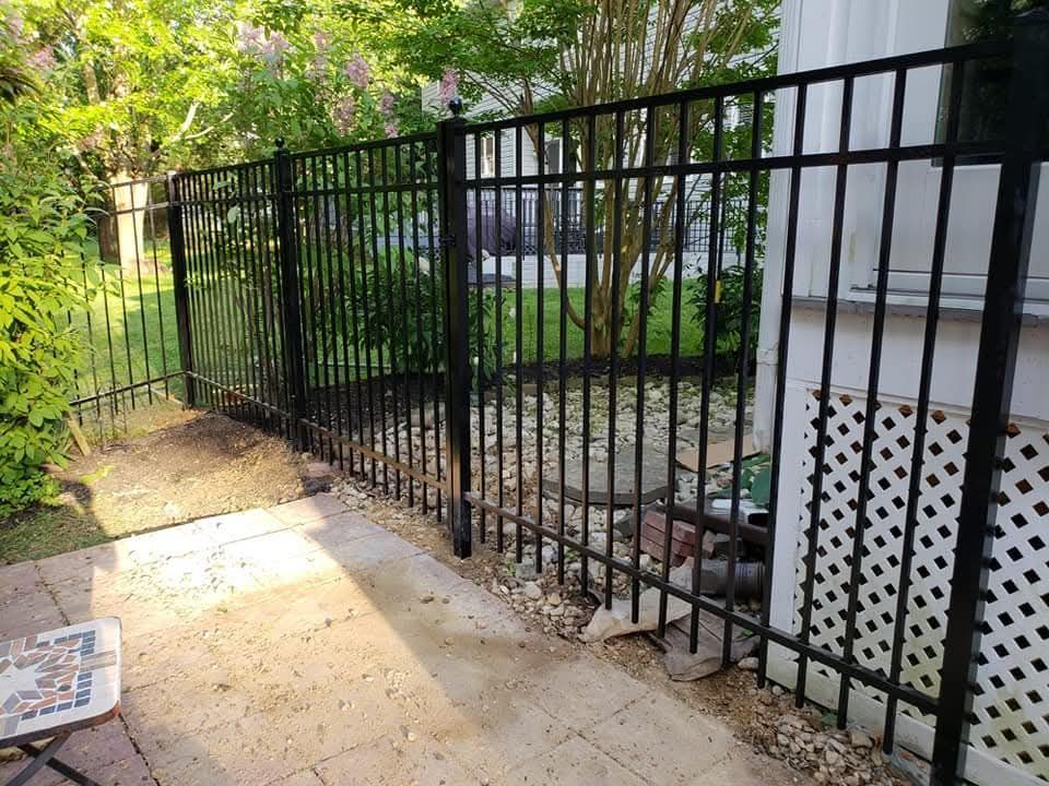 Black metal fence along a patio, with a white lattice panel and a garden in the background.