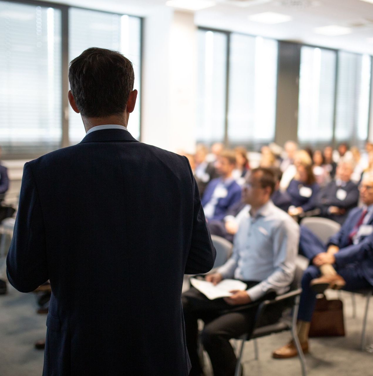 A man in a suit is giving a presentation to a group of people sitting in chairs.