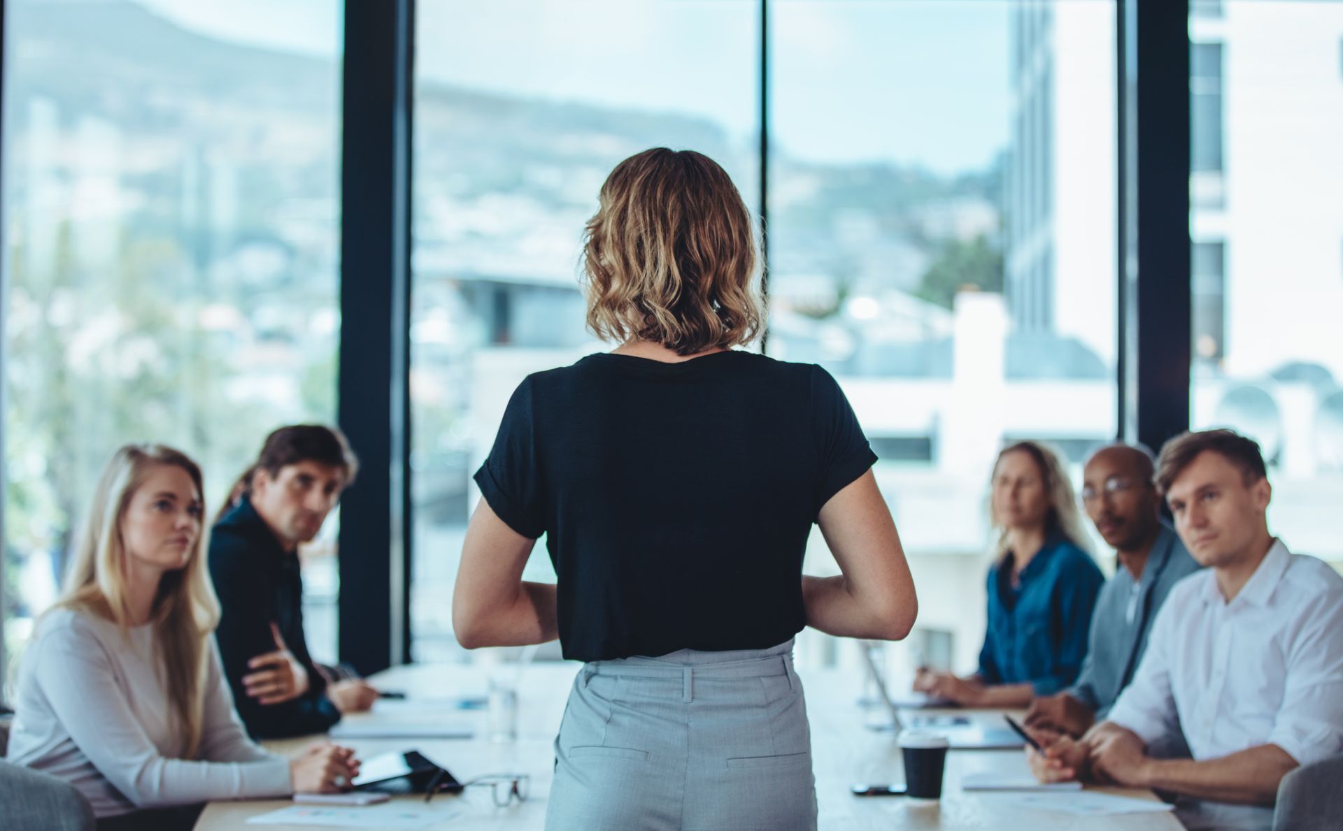 A woman is giving a presentation to a group of people sitting at tables.
